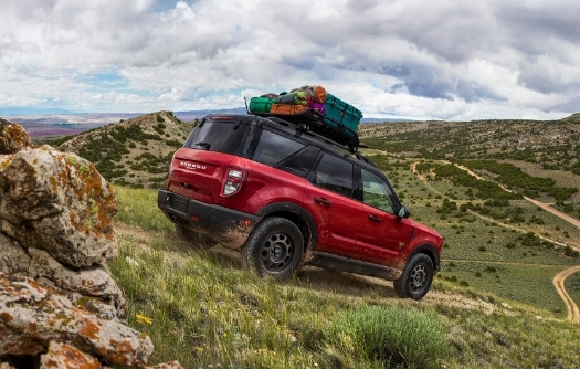 New Red Ford Bronco off-roading down hill with cargo on roof rack