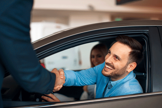 Customer sitting in the driver's seat and shaking hands with a Subaru salesman