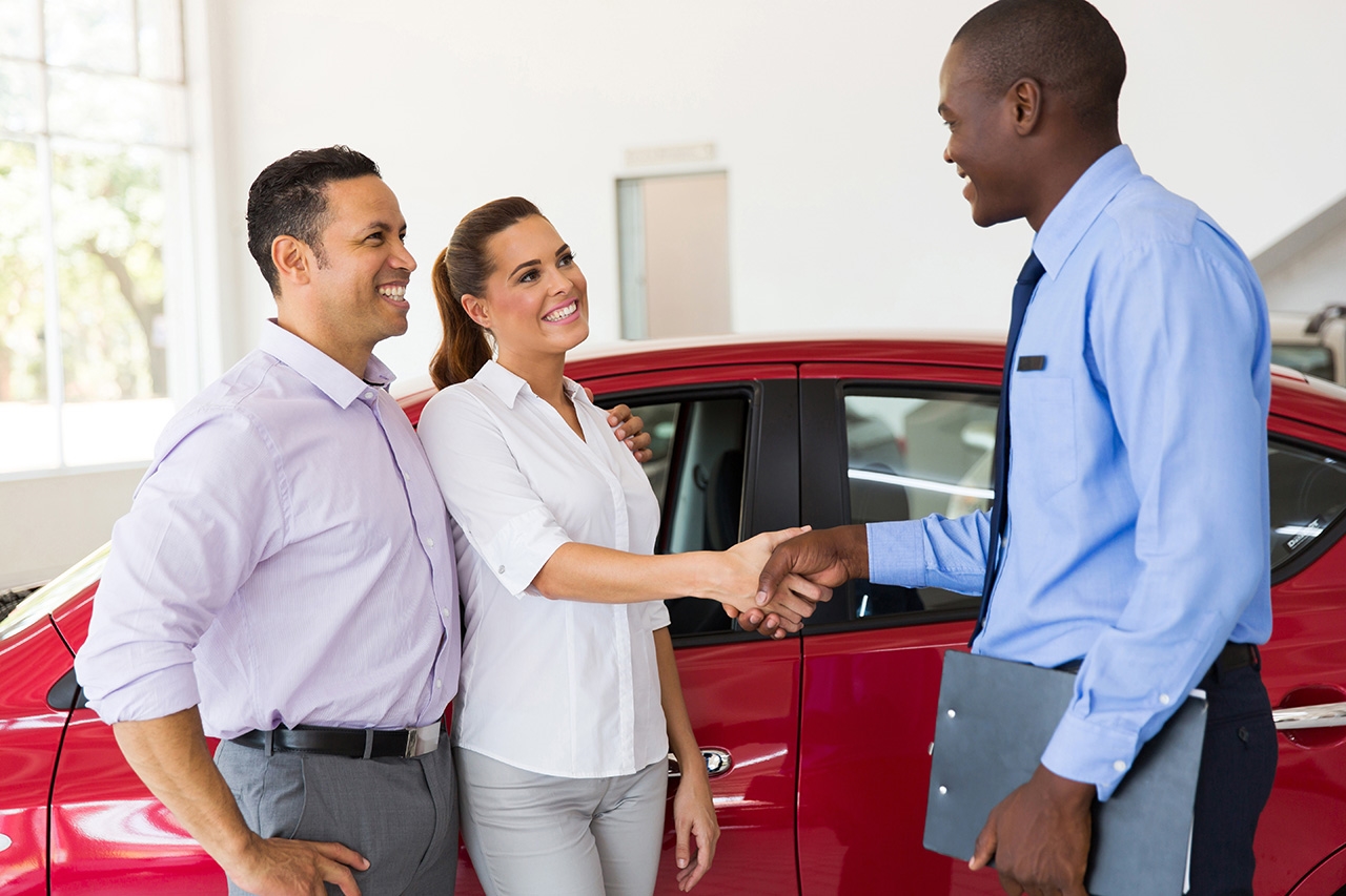 Couple shaking hands with a car dealer in a showroom