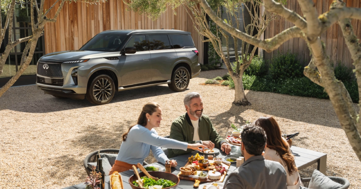 2026 INFINITI QX80 parked in a driveway while a family is on a picnic table nearby