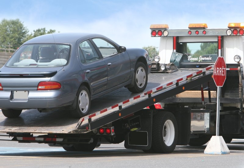 Roadside assistance towing a broken-down car onto a flatbed truck on a city street in Akron, OH