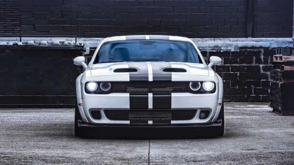 a front view of a white 2022 dodge challenger with black livery stripes parked outside a dark warehouse building