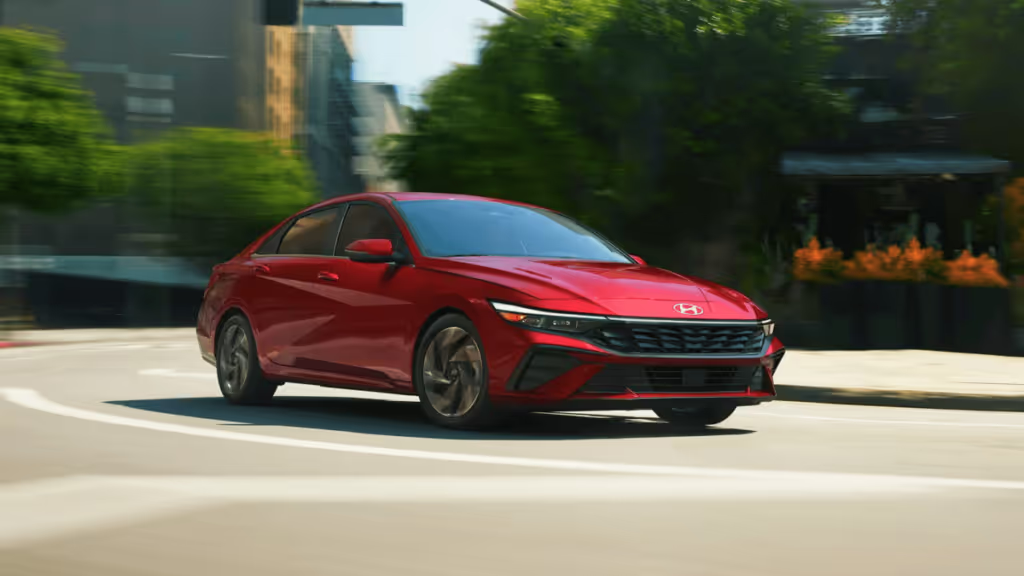 A red 2024 Hyundai Elantra compact sedan navigates a bustling city street, showcasing its sleek design and modern features.
