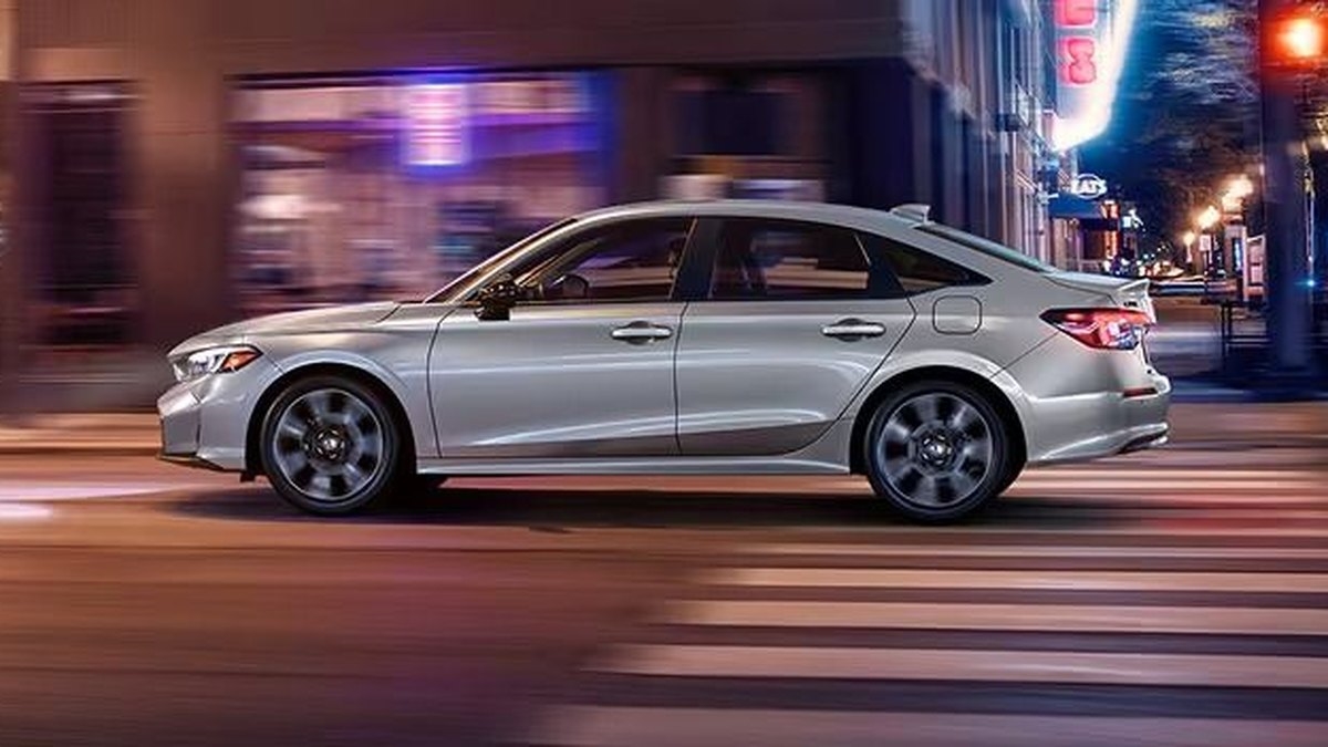 2026 Honda Civic Sport Touring Hybrid sedan in silver driving through a city intersection at night