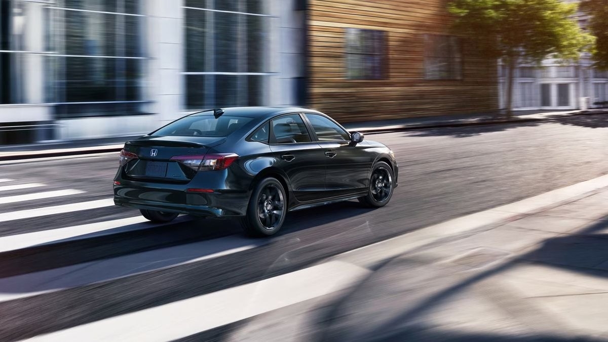 2026 Honda Civic Sport Hybrid sedan in black driving past a modern glass building