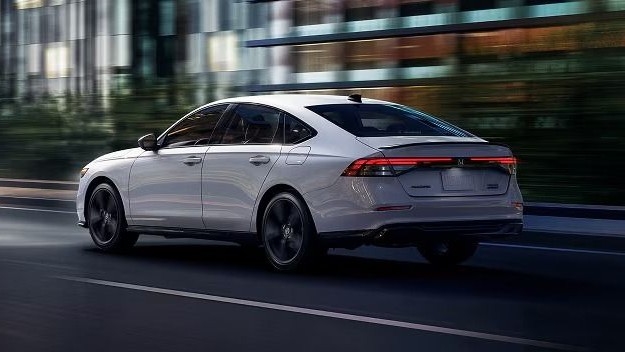 2026 Honda Accord Sport Hybrid sedan in white driving through a city street at dusk