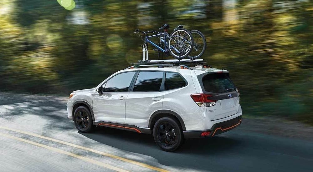 A white 2021 Subaru Forester Sport is shown driving on a tree lined road.