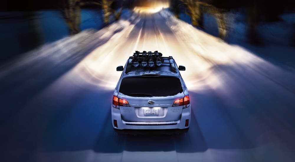 A white 2012 Subaru Outback is shown from the rear on a snowy path.