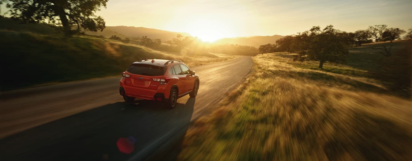 An orange 2018 Subaru Crosstrek Premium is shown from the rear driving on a sunny day.
