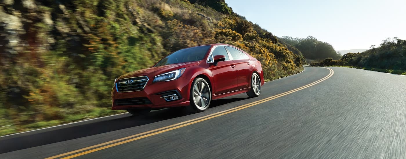 A red 2019 Subaru Legacy is shown from the side driving on an open road.