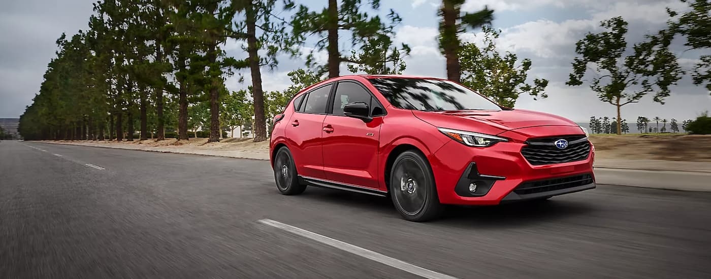 A red 2024 Subaru Impreza RS is shown driving on a tree-line road after leaving a Subaru dealer.