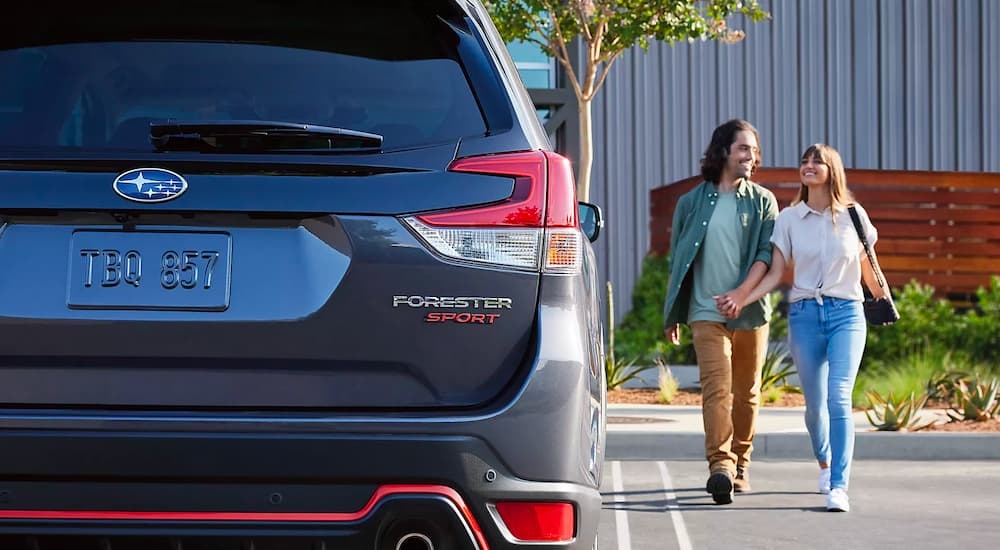 A couple holding hands next to a dark grey 2023 Subaru Forester Sport.