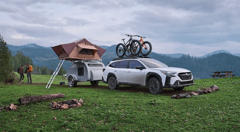 A white 2023 Subaru Outback Onyx Edition XT is shown towing a small camper at a remote site.