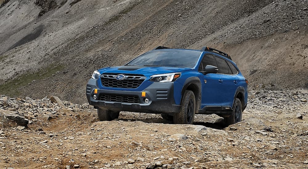 A blue 2023 Subaru Outback Wilderness is shown driving on a rocky dirt trail.