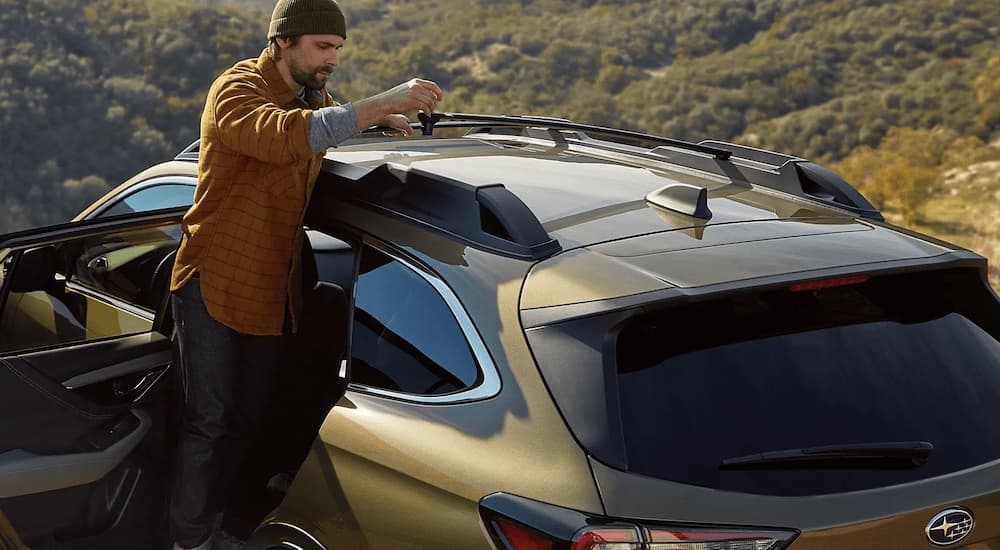 A man adjusting the roof rack on a green 2022 Subaru Outback after visiting a Subaru dealership in Red Hook.