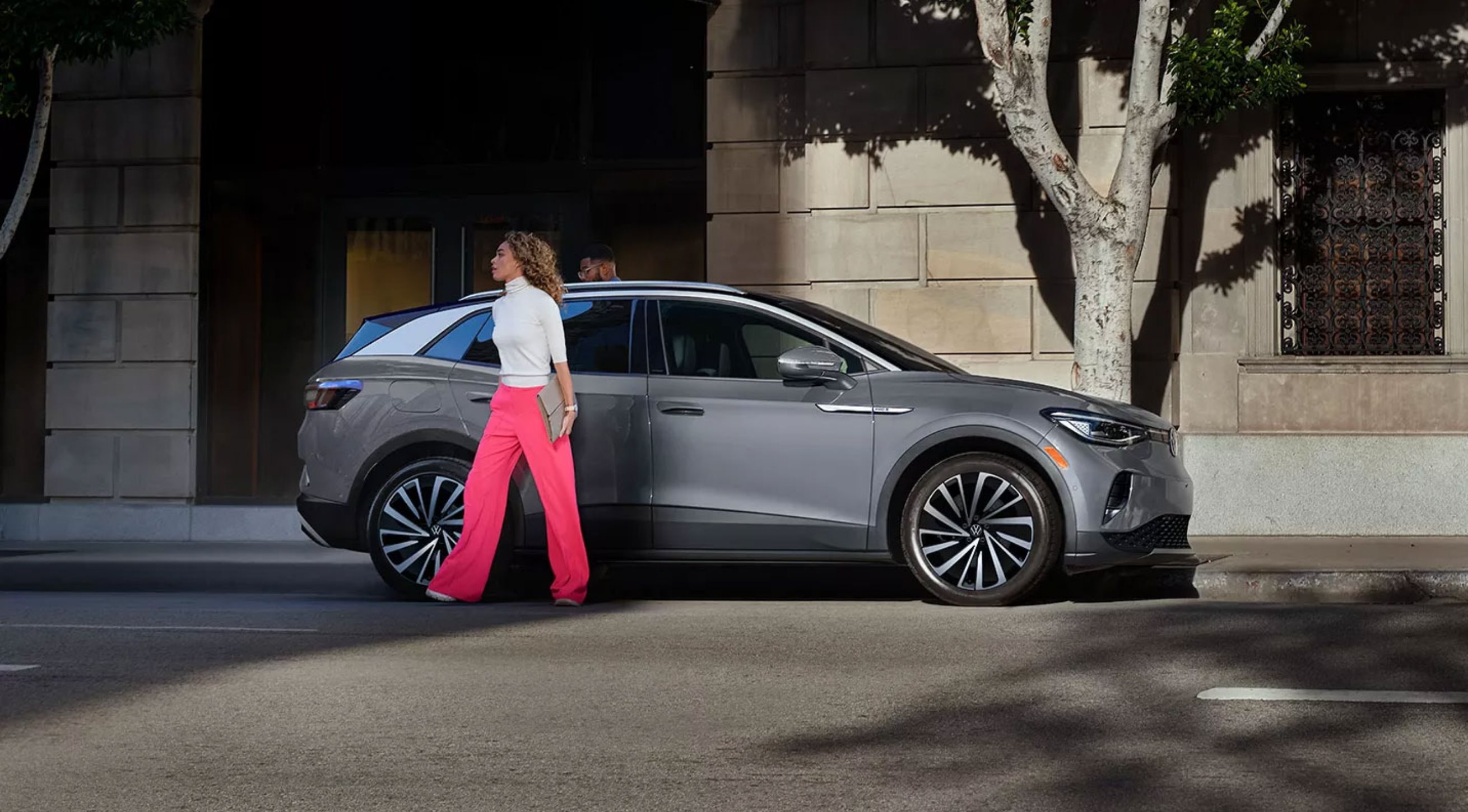 2023 Volkswagen ID.4 parked on city street with woman walking next to SUV.