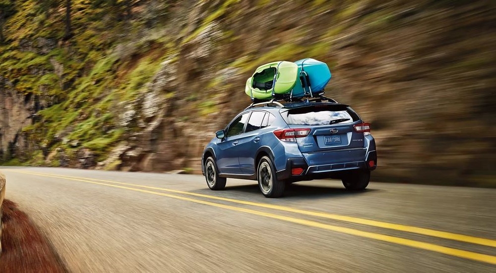 A blue 2023 Subaru Crosstrek Limited is shown driving on an open road with kayaks on the roof.