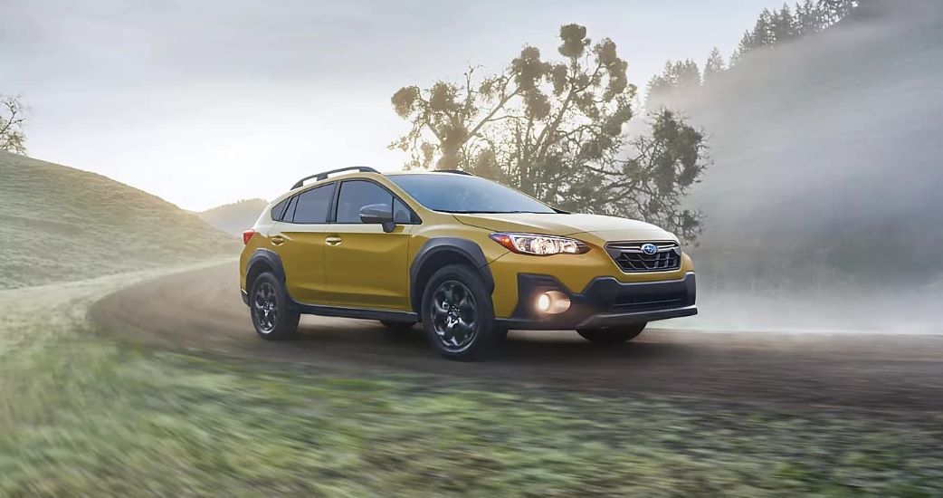 A yellow 2023 Subaru Crosstrek Sport is shown driving on a trail.