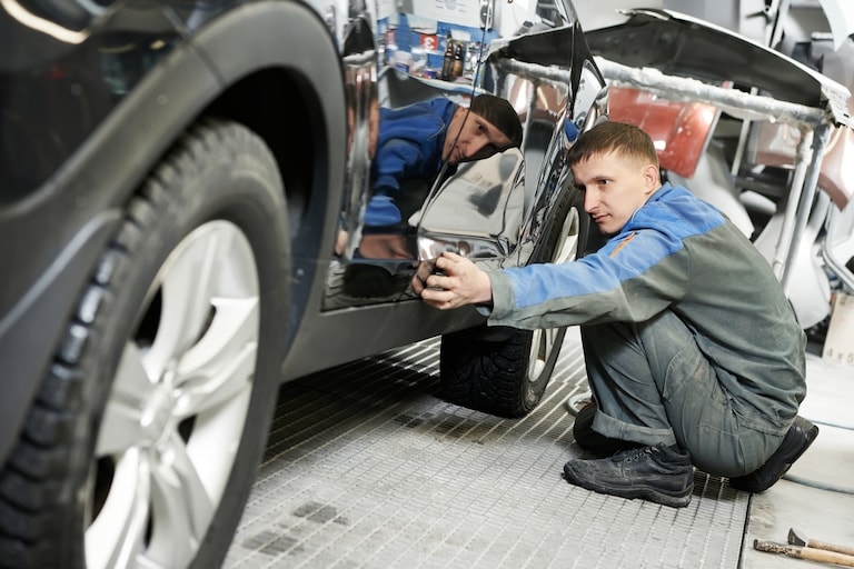 Technician at Landmark Fords Body Shop Looking Underneath A Tire to Diagnose an Issue and Repair it