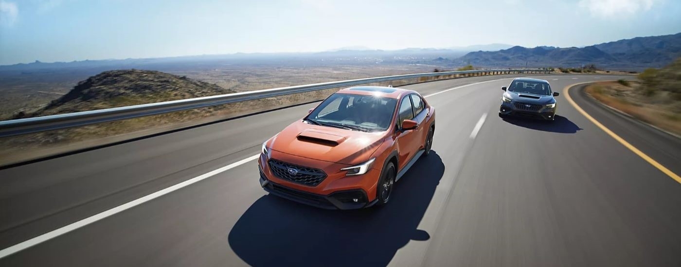 An orange 2023 Subaru WRX Limited and a black WRX GT are shown driving on a highway.