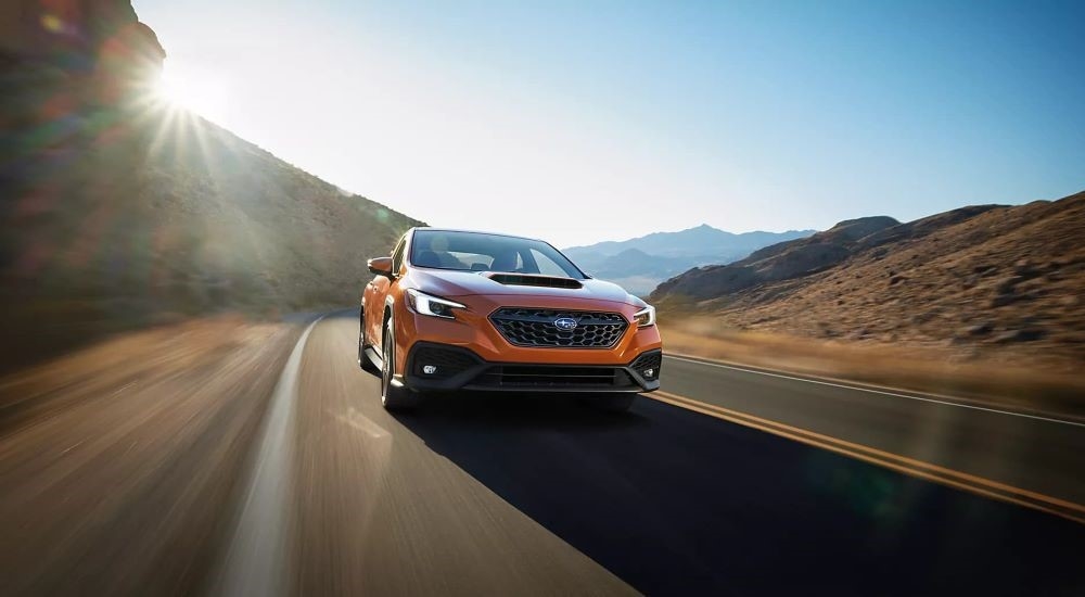 An orange 2023 Subaru WRX Limited is shown driving on a sunny day.