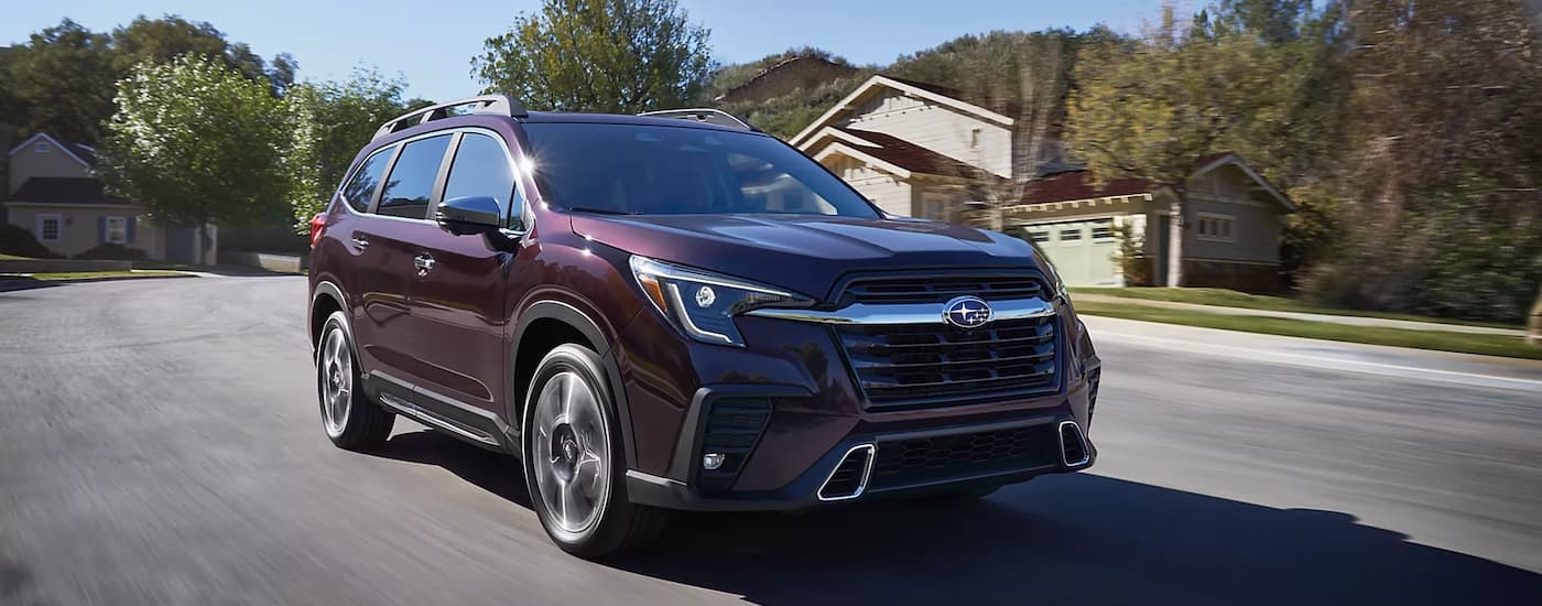 A red 2023 Subaru Ascent is shown driving through a quiet neighborhood.