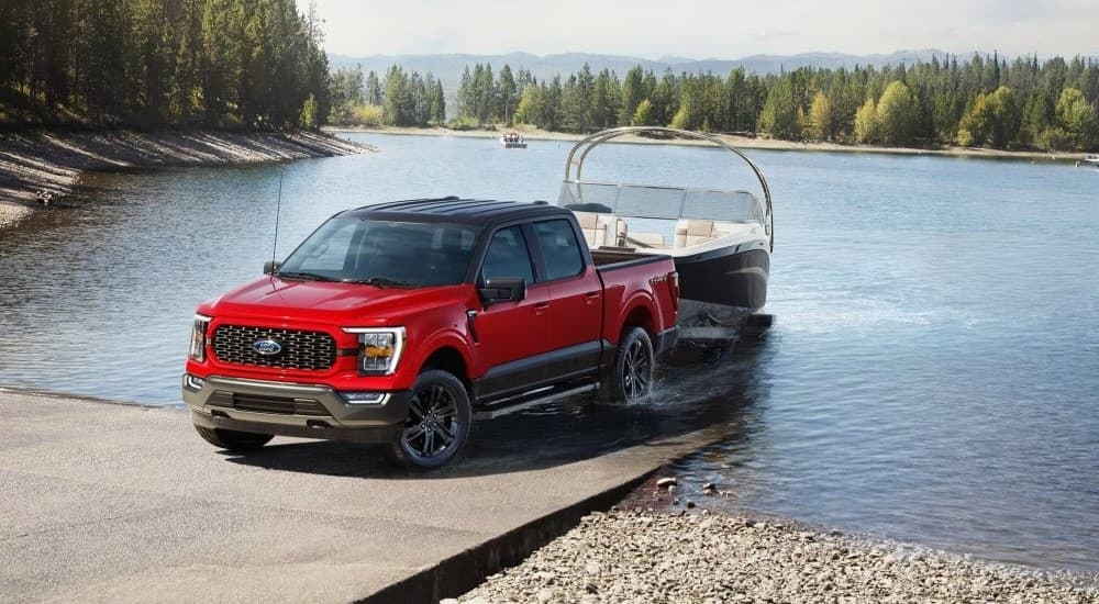 A red 2023 Ford F-150 XLT Heritage Edition is show towing a boat from a lake after visiting a Ford dealer near you.