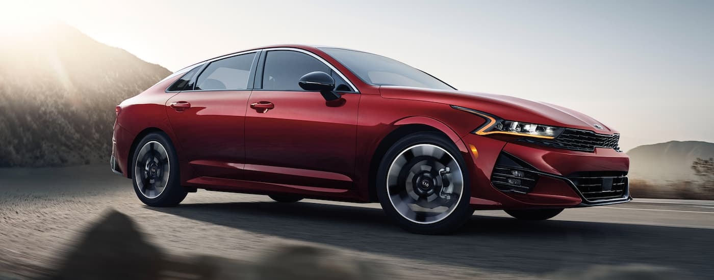 A red 2022 Kia K5 is driving on a winding mountain road.