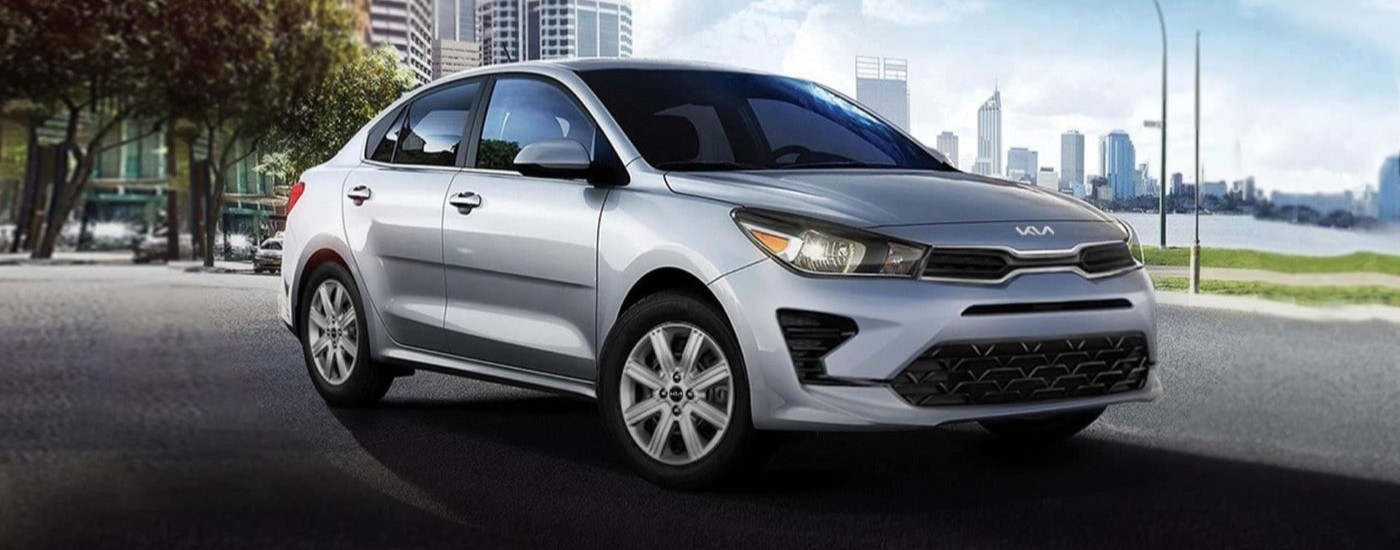 A silver 2023 Kia Rio is shown parked on a city street near a harbor.