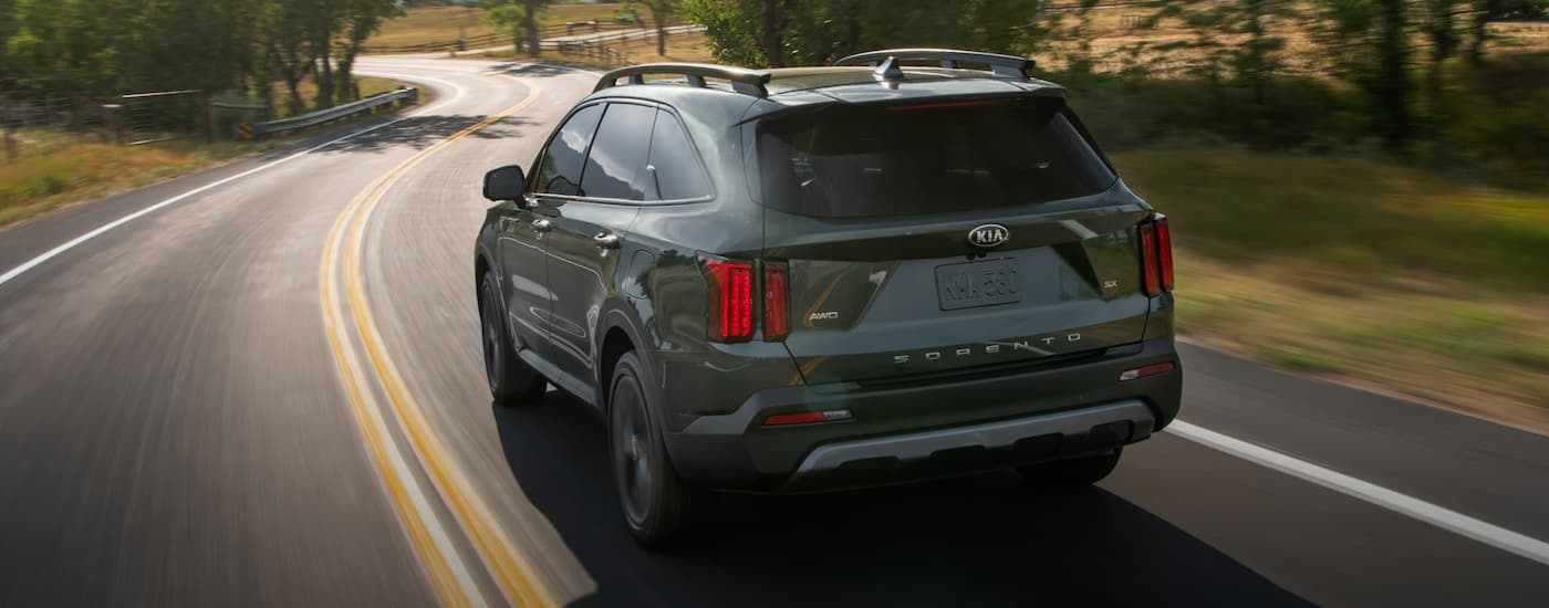 A green 2023 Kia Sorento is shown driving on a winding road.
