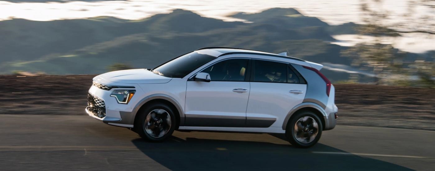 A white 2023 Kia Niro EV is shown from the side driving on a mountain highway.