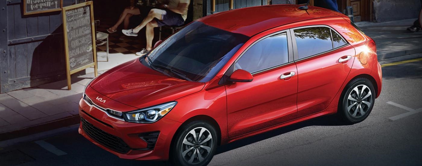 A red 2023 Kia Rio 5-Door is shown parked on the side of a city street.