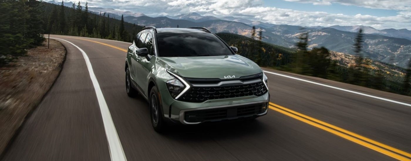 A green 2023 Kia Sportage is shown driving on a mountain highway.
