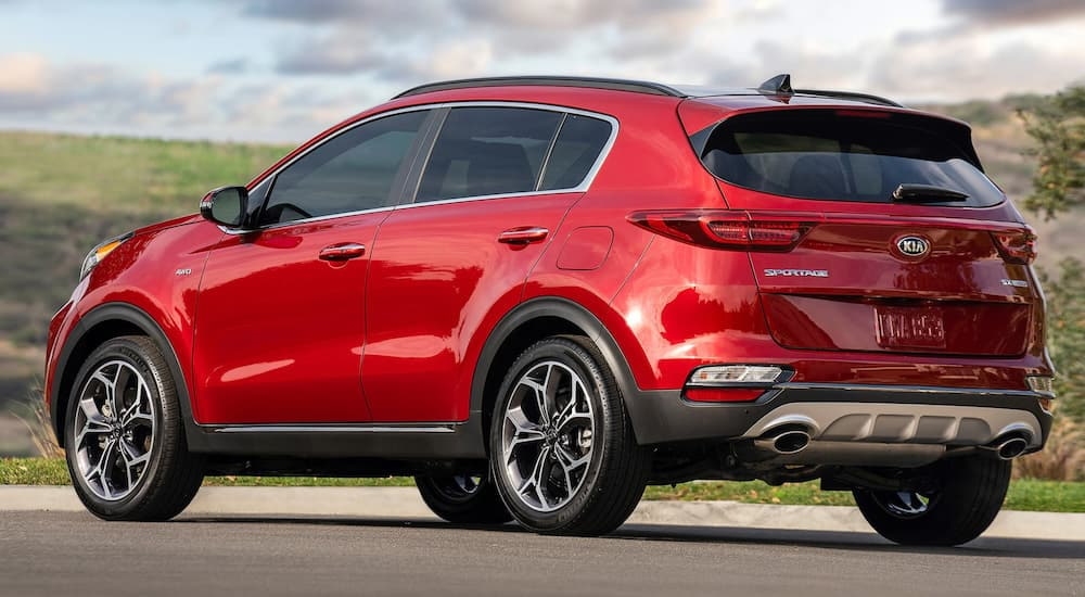 A red 2021 Kia Sportage parked on the side of a road by a grassy hill.