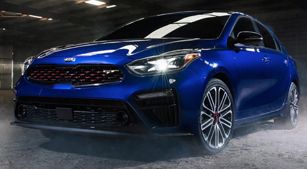 A blue 2020 Kia Forte parked in a garage near a used Kia dealership.