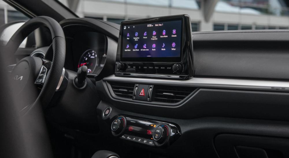 The black and silver interior of a 2023 Kia Forte with infotainment screen at a Kia dealership.