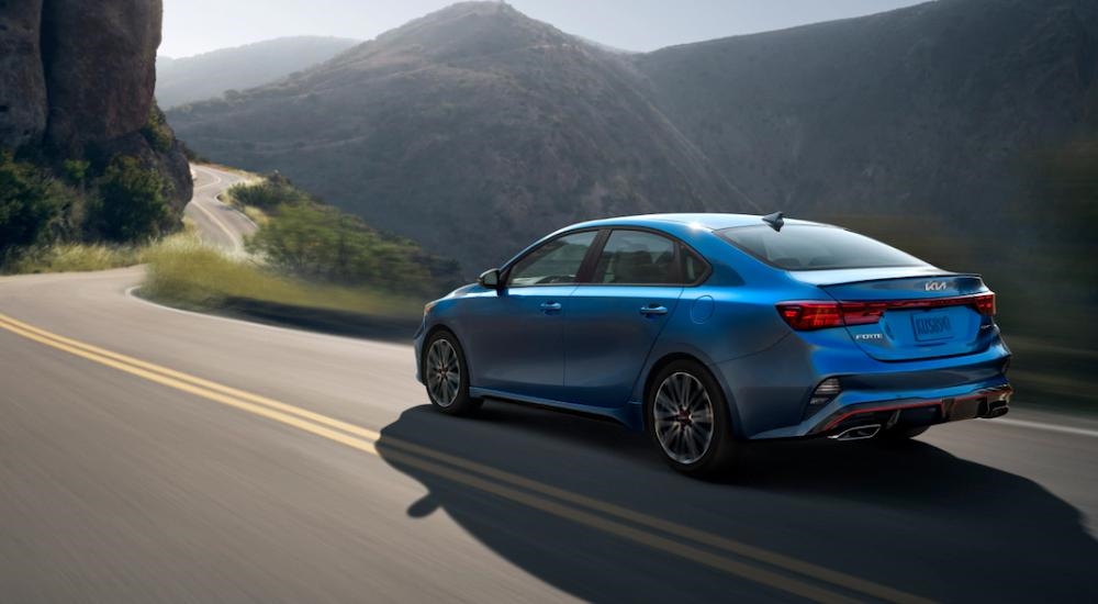 A blue 2023 Kia Forte GT driving on a winding highway through the mountains.