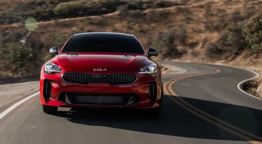 A red 2023 Kia Stinger is shown from the front driving on a winding road after visiting a Kia dealer in Victoria, TX.