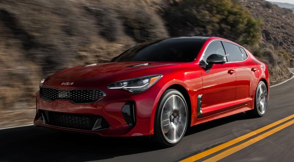 A red 2023 Kia Stinger driving on a desert road.