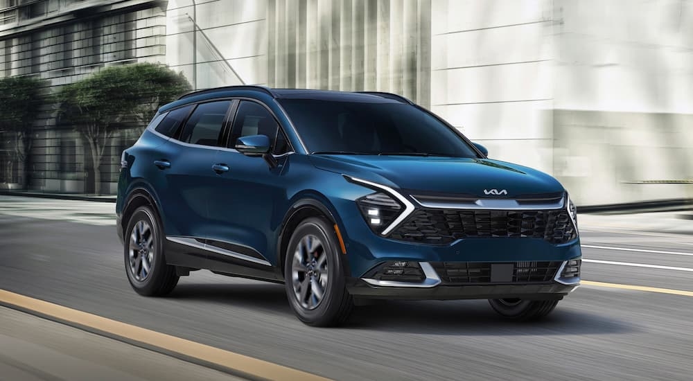 A dark blue 2023 Kia Sportage Hybrid driving on a city street after leaving a Kia dealership near Port Lavaca.