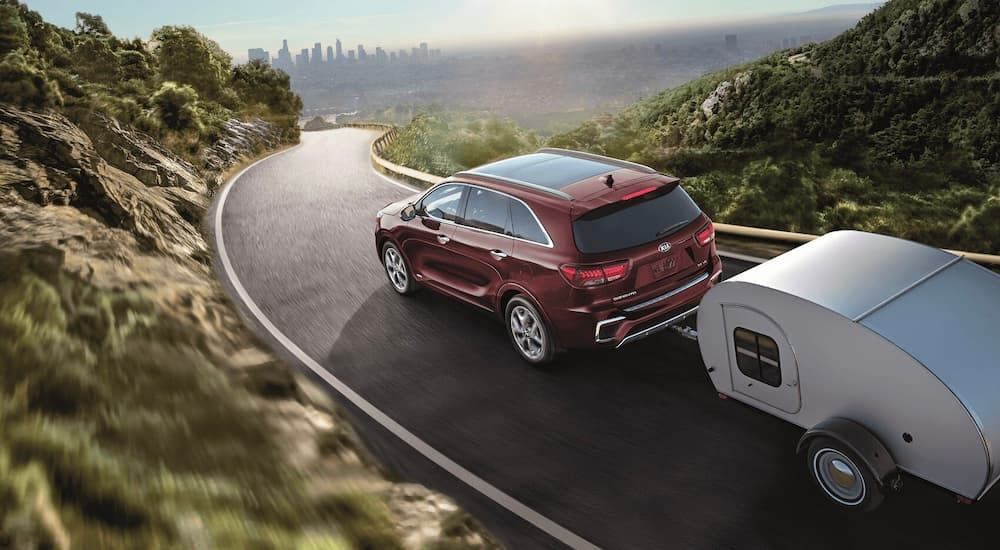 A red 2020 Kia Sorento towing a teardrop trailer on a mountain road.