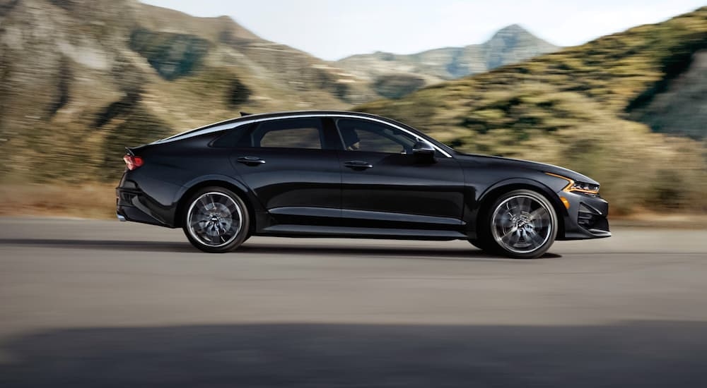 A black 2021 Kia K5 driving on a desert road.