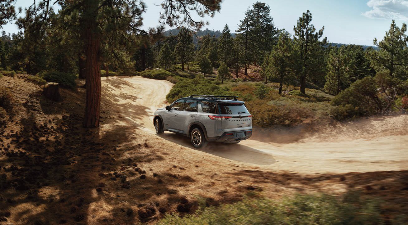 Women in window admiring 2024 Nissan Pathfinder on dirt road