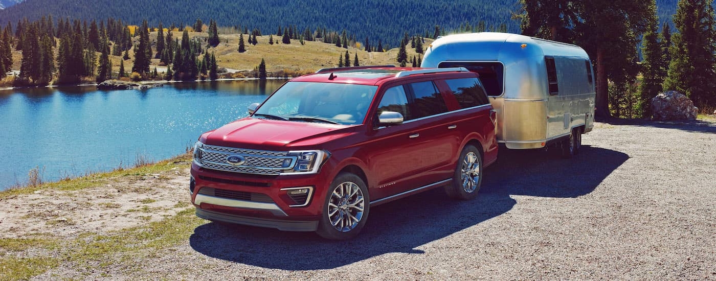 A red 2018 Ford Expedition is shown towing an Airstream trailer near a lake.
