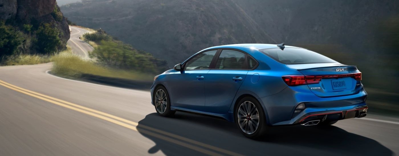 A blue 2022 Kia Forte is shown driving on a mountain road after looking at used car sales.
