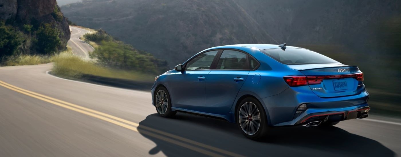 A blue 2022 Kia Forte is shown driving on a mountain road after looking at used car sales.