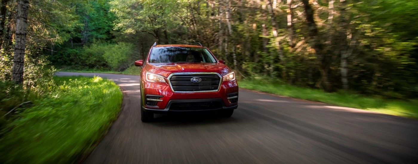 A red 2020 Subaru Ascent is shown from the front driving on a tree-lined road.