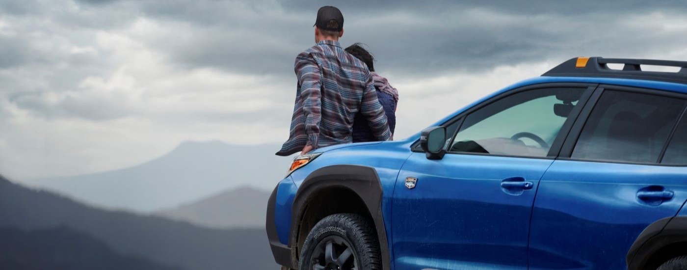 People are shown leaning against a blue 2022 Subaru Outback Wilderness at an overlook.