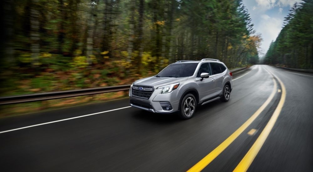A silver 2023 Subaru Forester is shown driving on a tree-lined road after leaving a car dealer near Poughkeepsie.