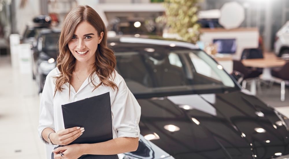 A smiling saleswoman at a dealership specializing in used car sales.
